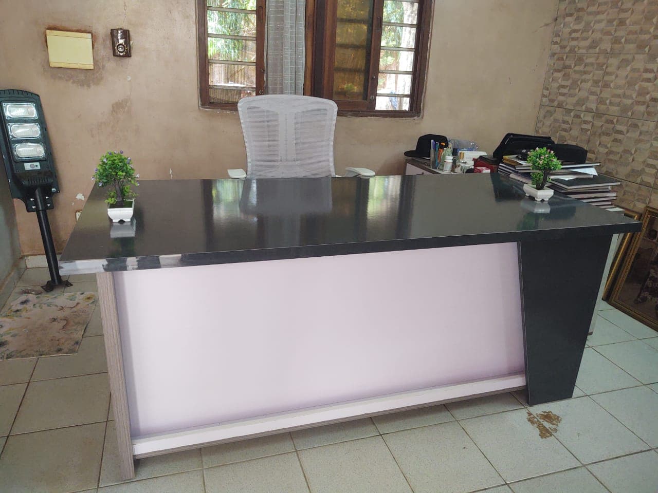 Bureau moderne avec plateau noir, chaise ergonomique grise et deux petites plantes vertes en pot.