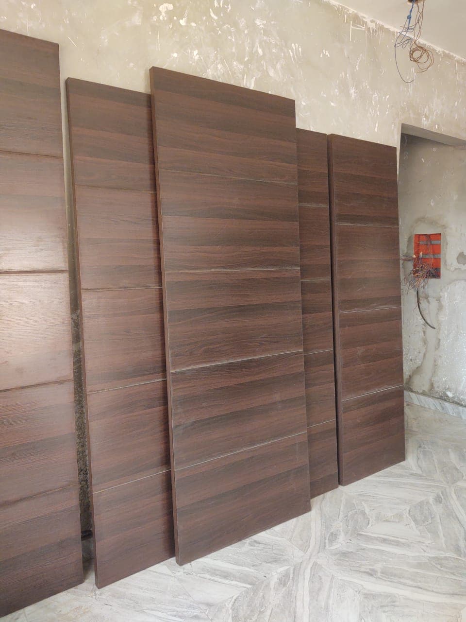 Plusieurs portes en bois brun foncé appuyées contre un mur en cours de rénovation.