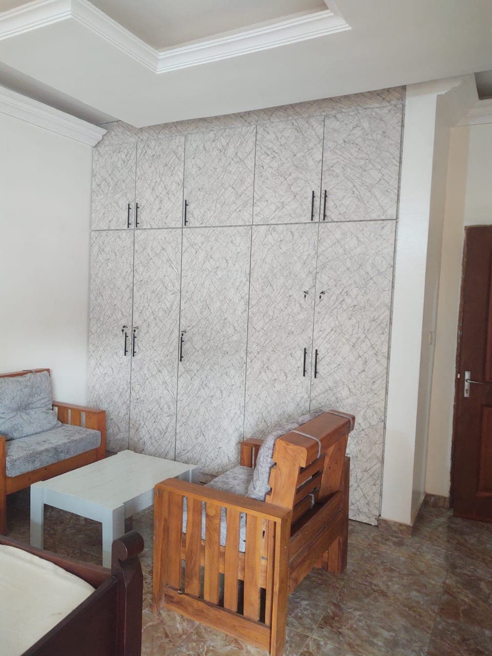 Armoire murale à motif marbré blanc derrière des fauteuils en bois et table basse.