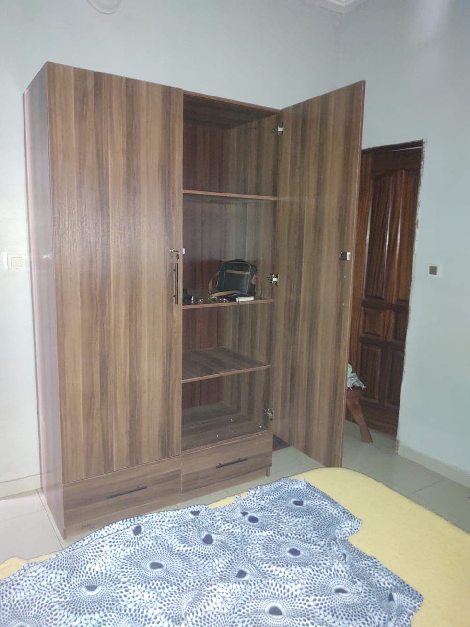 Armoire en bois avec une porte ouverte révélant des étagères et deux tiroirs inférieurs.