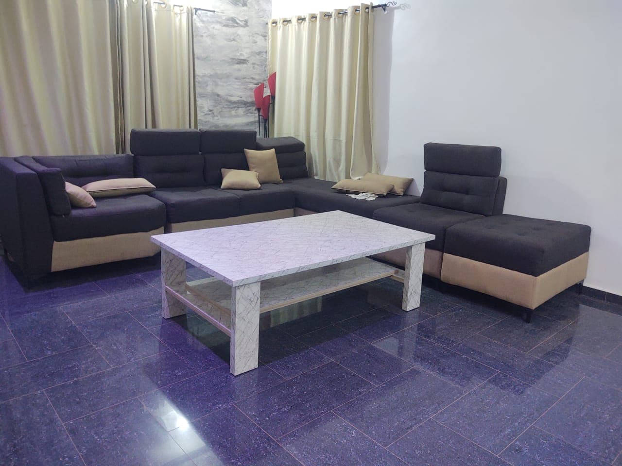 Canapé d'angle gris et beige, table basse en marbre blanc et sol carrelé violet.