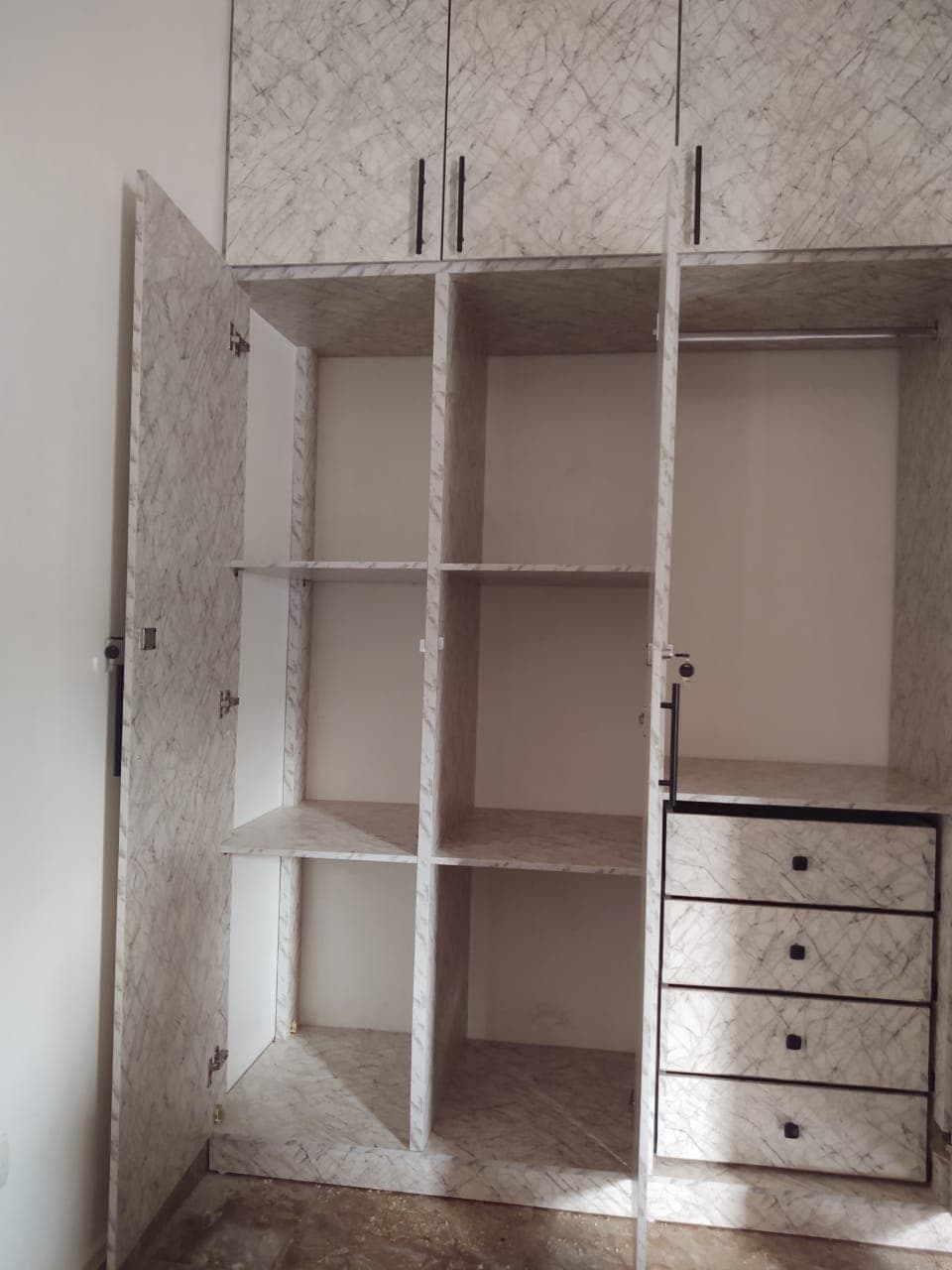 Armoire ouverte à motif marbre gris avec étagères, penderie et quatre tiroirs de rangement.